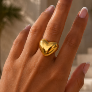 Gouden stainless steel Big Heart Ring met groot glanzend hart gedragen om de hand van een zongebruinde vrouw met French manicure nagels.