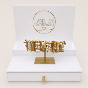 Luxe Label Six B2B armbanden display met gouden en witte kralenarmbanden op een stijlvolle witte sieradendisplay voor winkels en boutiques.